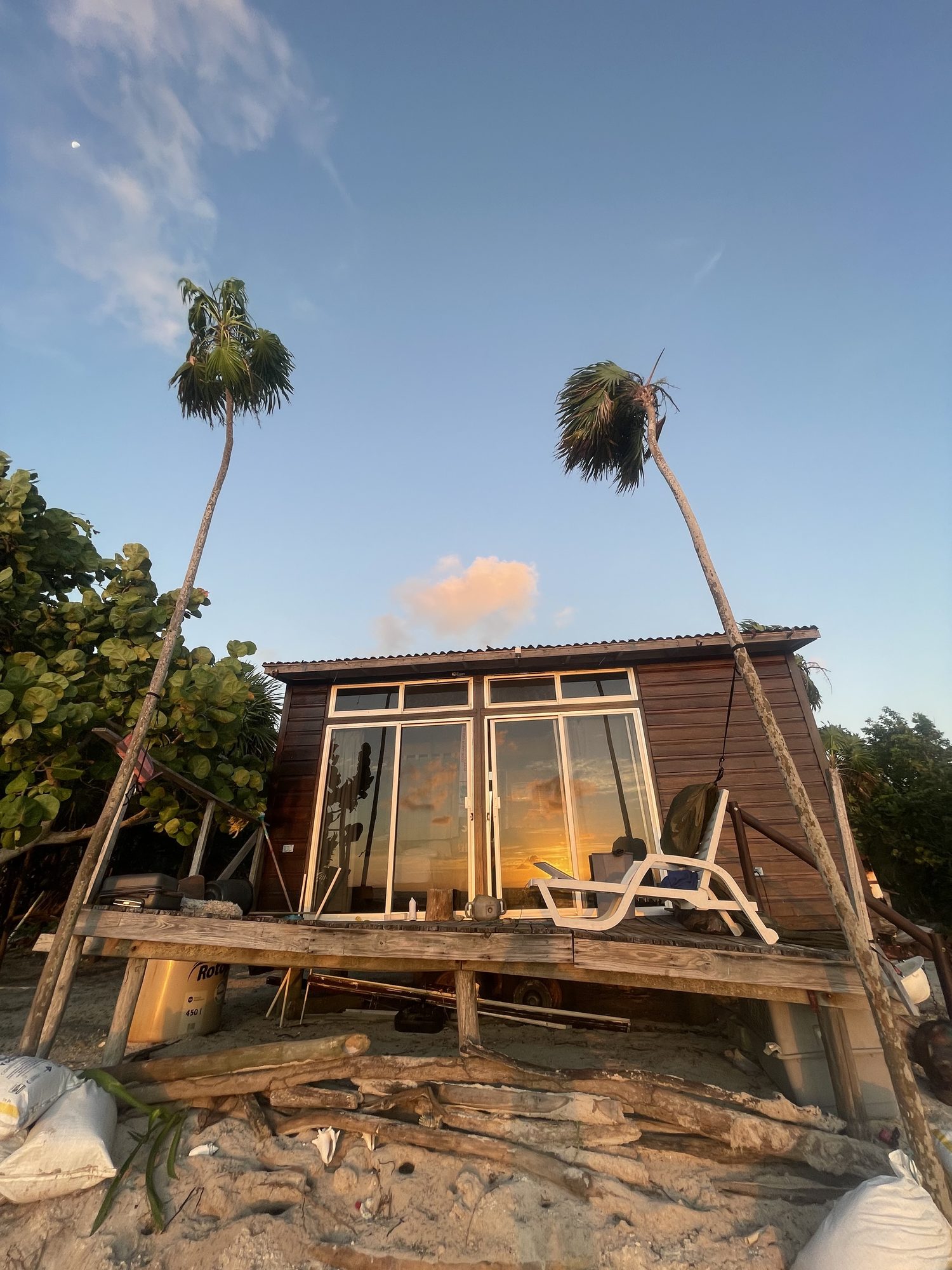 The casa pequeña at golden hour, framed by two tall palms on a quiet stretch of beach.