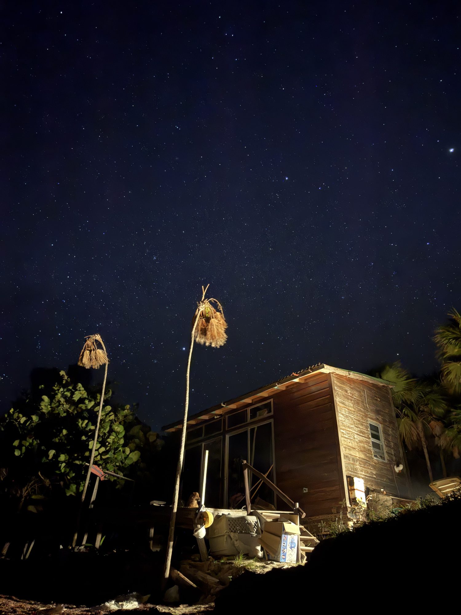 The casa at night, lit warmly from inside, two woven lanterns hanging in the foreground under a sky full of stars.