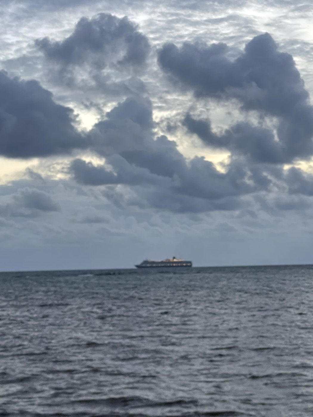 A small ship far on the horizon, dwarfed by a piled-up bank of dark cloud.
