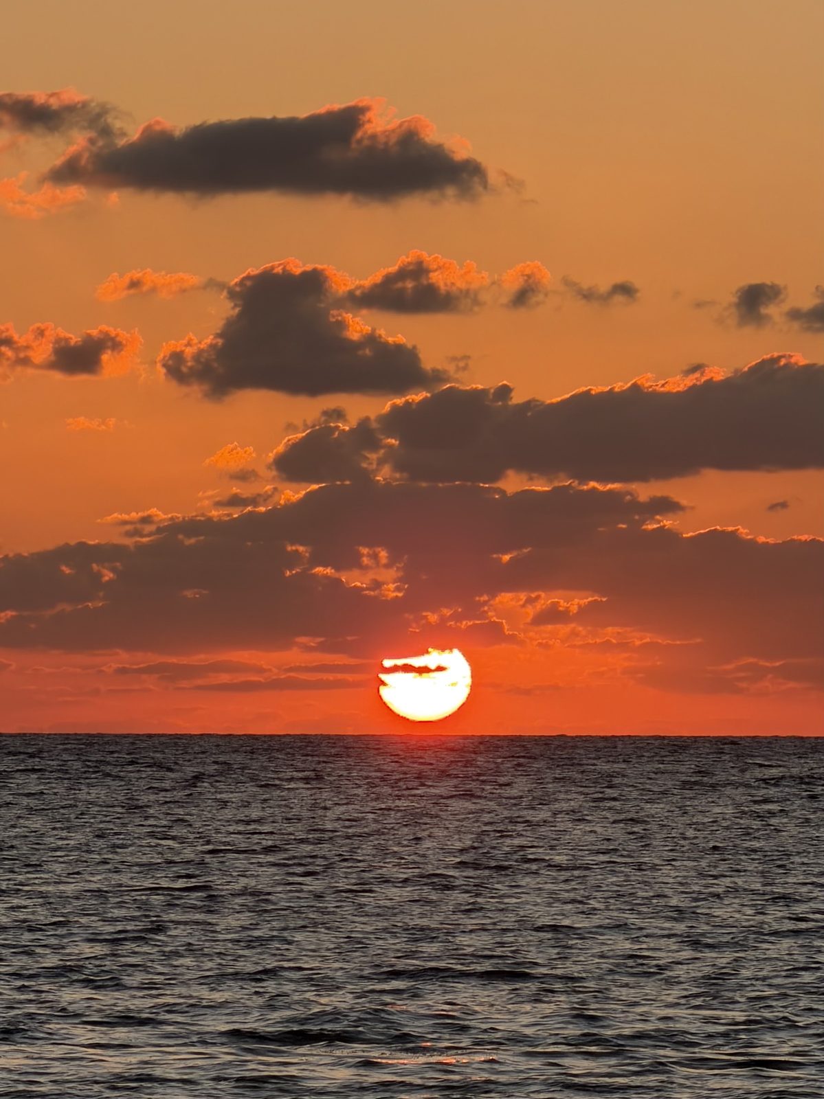 The sun rising over the Caribbean, low cloud bands lit orange and red.